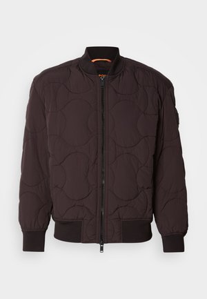 Veste bombardier matelassée marron foncé avec zip à l'avant, poignets et col côtelés, et motifs de couture circulaires subtils.