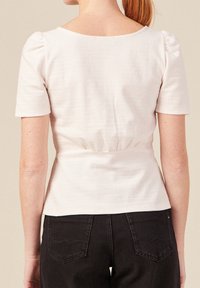 Top bianco testurizzato con maniche a sbuffo corte, vita aderente e scollatura tonda, abbinato a pantaloni in denim scuro con tasche posteriori.