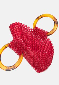 Röd pärlhandväska med bärnstensfärgade cirkulära handtag, med en strukturerad, vävd design och en distinkt form som liknar ett hjärta.