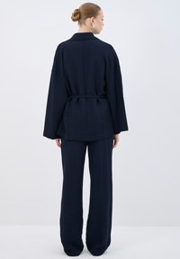 Navy two-piece outfit featuring a loose-fitting, textured top with a collar and a cinched waist, paired with wide-leg trousers.
