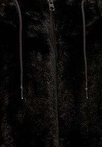 Primer plano de una chaqueta de forro polar negro suave con cremallera central y dos cuerdas negras colgando.