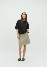 Black cropped sweatshirt with short sleeves paired with a beige wrap skirt featuring a pocket and a circular button detail. Black flat shoes.
