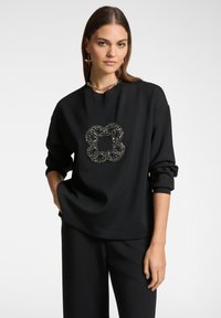 Felpa nera realizzata in materiale morbido, con un design floreale decorativo in perline sul davanti e ampi polsini, abbinata a pantaloni neri.