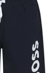 Shorts de bain navy avec une taille élastique à cordon, présentant un grand logo blanc imprimé verticalement sur le côté. Texture lisse, tissu léger.
