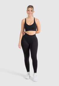 Reggiseno sportivo nero e leggings a vita alta, entrambi realizzati in tessuto elastico e morbido. Scarpe da corsa bianche completano l'outfit.