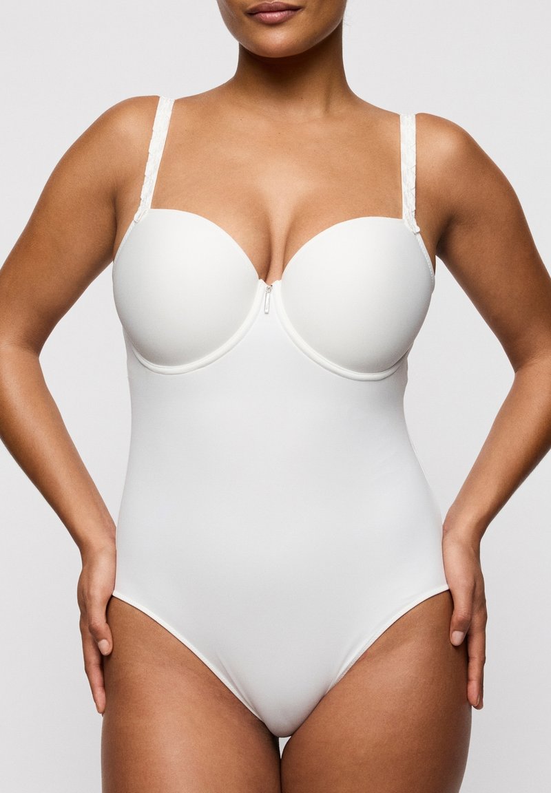 Donna che indossa un body modellante intero bianco con spalline regolabili, in piedi con le mani appoggiate sui fianchi, sfondo neutro.