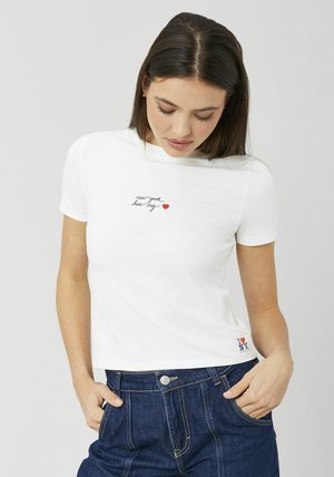 T-shirt blanc en coton avec un texte en script « new york has my » et un graphique en forme de cœur rouge. Short en denim bleu marine avec des coutures visibles.