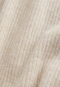 Miękka beżowa dzianina prążkowana z delikatną pionową teksturą dziania, ukazująca łagodne fałdy i subtelne zróżnicowanie kolorów na całej powierzchni materiału.