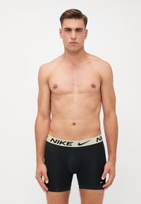 Sorte Nike-boxershorts med en lys grøn elastik i taljen, der har logo-detaljer. Glat tekstur, tætsiddende pasform og design der går til midten af låret.