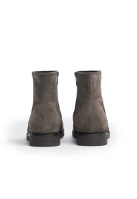 Botas de ante gris hasta el tobillo con una textura suave, que presentan una puntera redondeada y una suela de goma texturizada baja. Detalle de cremallera en los laterales.