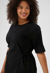 Top negro de manga corta con cuello redondo, cintura ajustada con lazo y tela suave con una textura sutil.