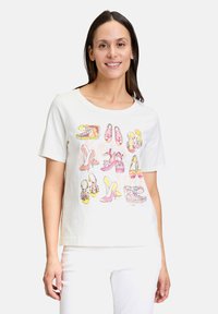 Baumwoll-T-Shirt mit Rundhalsausschnitt, das auf der Vorderseite bunte Schuhillustrationen in verschiedenen Stilen zeigt. Weißer Stoff, kurze Ärmel.