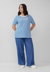 Blau-weiß gestreiftes T-Shirt mit "dream" Stickerei, kombiniert mit lockeren, jeansähnlichen Hosen, weißen Sneakers und einem schlichten runden Ausschnitt.