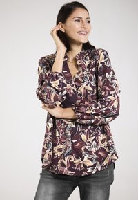 Langärmlige Bluse in Burgunderrot mit floralem Muster in Creme und Blau. Verfügt über einen lockeren Schnitt und elastische Bündchen. Glatte Stoffstruktur.