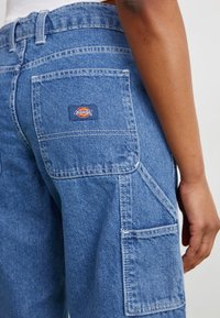 Mėlynos džinsinės kargo kelnės su etiketės aplikacija ant galinio kišenės. Su daugybe kišenėmis ir laisvu siluetu. Textūruotas audinys.