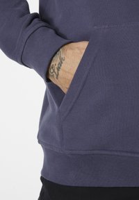 Sudadera púrpura de manga larga, con puños acanalados y un bolsillo frontal. Textura suave y color sólido, con detalles de costura limpia.