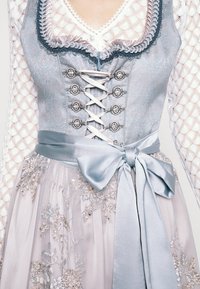 Tenue traditionnelle composée d'un corsage bleu clair avec des détails en dentelle et des éléments argentés, accompagné d'une jupe fluide ornée de broderies florales et d'un nœud en satin.