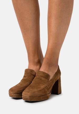 Brown suede platform loafers with a block heel, featuring a rounded toe and a decorative stitched accent on the vamp.