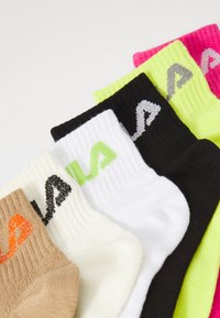 Cinco pares de calcetines en varios colores: beige, blanco, negro, verde neón y rosa. Cada par presenta una textura en relieve y un logo.