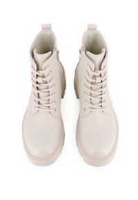 Botines beige con cierre de cordones, material de cuero liso, puntera redonda y cremallera lateral. Presentan una suela robusta y un diseño que llega hasta el tobillo.