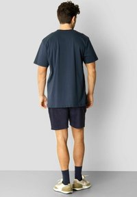 Marineblå t-skjorte med korte ermer, rund hals og en avslappet passform, sammen med mørke shorts og joggesko med lyse detaljer.