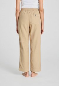 Pantalones de color beige, holgados, con una cinturilla elástica y cordón. Cuentan con un bolsillo trasero y dobladillos ajustados para un aspecto y sensación relajados.
