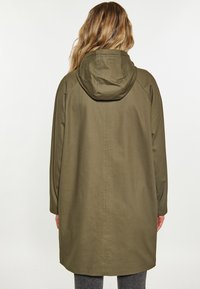 Cappotto verde oliva con cappuccio dal design semplice, maniche lunghe e taglio dritto. Presenta una texture morbida e dettagli di cucitura visibili.