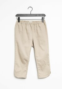 Pantalons beige ajustés en tissu doux et léger. Ils possèdent une taille élastique et un ourlet avec de petites fentes sur les côtés. Accrochés à un cintre noir.