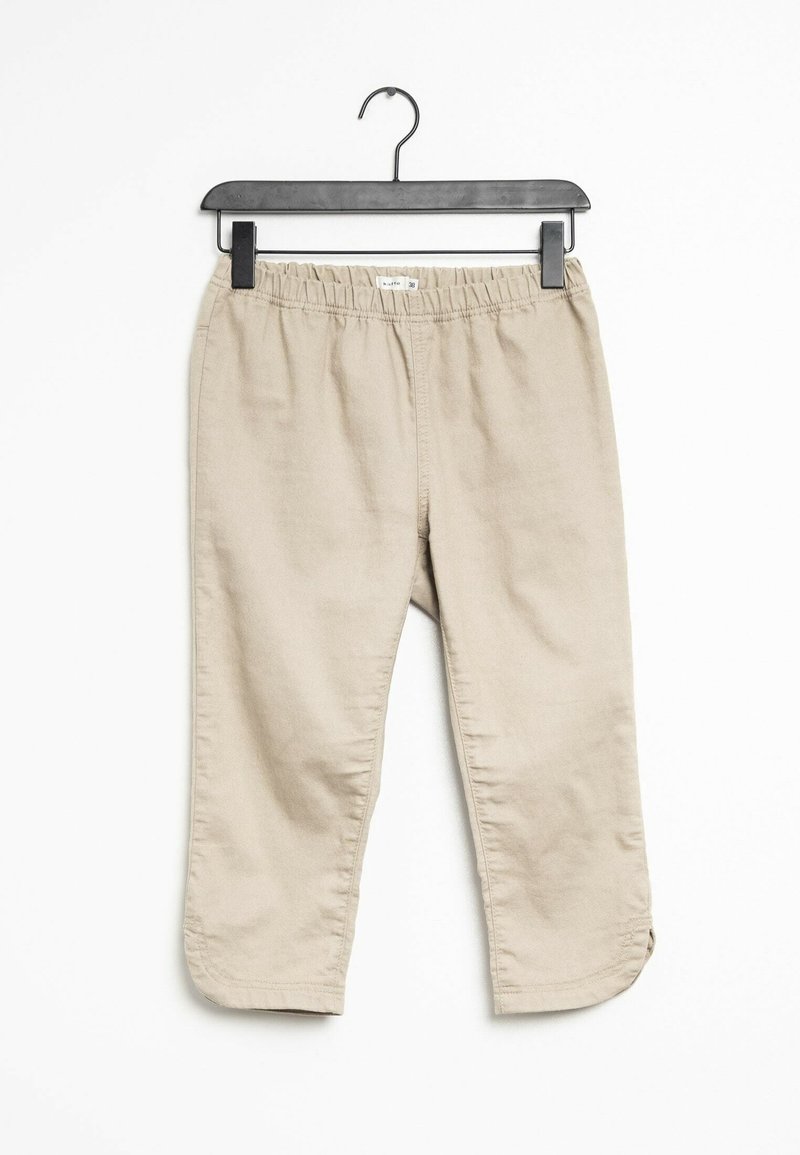 Pantalons beige ajustés en tissu doux et léger. Ils possèdent une taille élastique et un ourlet avec de petites fentes sur les côtés. Accrochés à un cintre noir.