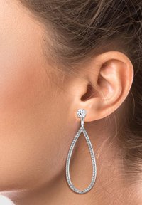 Silberne Tropfenohrringe haben eine tropfenförmige Silhouette mit einer glänzenden Oberfläche, verziert mit kleinen klaren Kristallen oben und entlang des Randes.