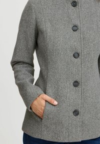 Manteau en mélange de laine gris avec cinq boutons noirs, poches latérales, silhouette ajustée et col structuré. Texture douce et finition lisse.