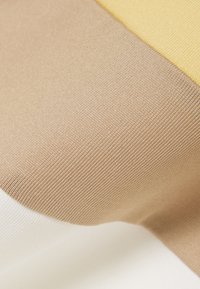 Gros plan d'un tissu à texture lisse et tissée serrée présentant des blocs de couleur diagonaux beige, jaune et blanc.