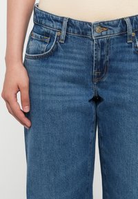 Lys blå denimjeans med en avslappet passform, som har fem lommer, knappestengning, subtile sømdetaljer og en glattere tekstur.
