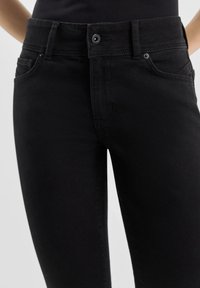Schwarze Denim-Jeans mit tailliertem Design, ausgestattet mit einem Knopfverschluss, fünf Taschen und Kontrastnähten auf einer gleichmäßigen Textur.