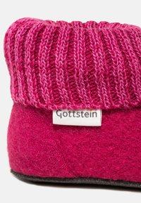 Fuchsia uldesko med en ribbet strikket krave. Har et hvidt mærke med "Gottstein". Blød tekstur og rund form, velegnet til indendørs brug.