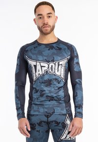 Hosszú ujjú sportpóló tengerészkék és szürke álcázásban, nagy fehér "TAPOUT" logóval az elején és lélegző anyag kialakítással.