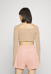 Top cropped de manga longa em tecido canelado bege, emparelhado com calções rosa com padrão. O top tem um decote quadrado e mangas bufantes, e os calções têm uma cintura elástica.