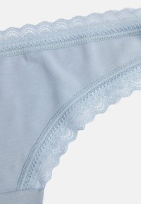 Lichtblauwe katoenen string met een delicate kantafwerking langs de tailleband, met een golvende rand en een gladde textuur overal.