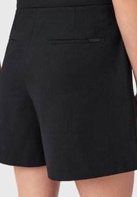 Zwarte shorts hebben een verfijnd ontwerp met een soepele textuur, achterzakken en een klein merketiket dicht bij de rechterzak.