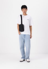 Bolso cruzado negro con textura suave y cierre de cremallera, combinado con una camiseta blanca y jeans de un azul claro, que presentan un corte relajado.