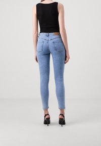 Jeans ajustados de color azul con una cintura alta, un ligero desgastado y bolsillos traseros. Combinados con una blusa sin mangas negra y sandalias negras de tacón.