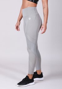 Leggings gris taille haute avec des accents en maille, des panneaux texturés et une coupe ajustée, assortis à des chaussures de sport noires.