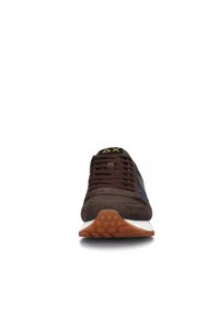 Sneaker in suede marrone con accenti blu, punta arrotondata, lacci marroni, suola intermedia bianca e suola in gomma testurizzata con motivi circolari.