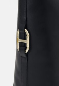 Zwarte leren handtas met een goudkleurige gesp, een gladde textuur en een gestructureerd ontwerp. Inclusief een zijriem bevestiging.