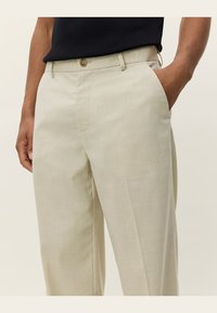 Beige tailored trousers made of lightweight fabric, featuring a flat front, side pockets, and a single button closure at the waist.
