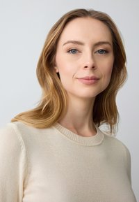 Maglione beige a maglia con scollatura rotonda e bordo a coste, caratterizzato da una texture morbida e un design minimalista, indossato da una persona con capelli lunghi.