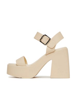 Sandalia de plataforma beige con tacón ancho, tiras abiertas en la punta y correa en el tobillo con hebilla plateada.