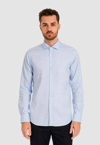 Camicia a maniche lunghe azzurro chiaro con chiusura a bottoni, colletto classico e un tessuto liscio e texture. Accentata da bottoni bianchi.
