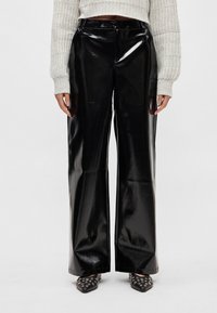 Calças pretas brilhantes de perna larga feitas de couro sintético; apresentam cintura alta e textura lisa e reflectora.