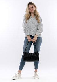 Schwarze Lederhandtasche mit weicher, runder Form und einer dezent strukturierten Oberfläche. Das Modell trägt ein gestreiftes Oberteil und blaue Jeans.